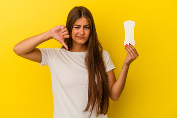 Young caucasian woman holding a compress isolated on yellow background showing a dislike gesture,...