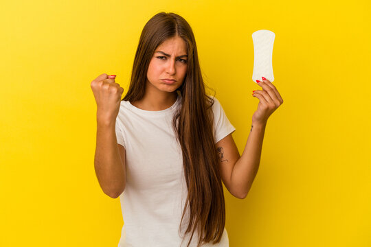 Young caucasian woman holding a compress isolated on yellow background showing fist to camera, aggressive facial expression.