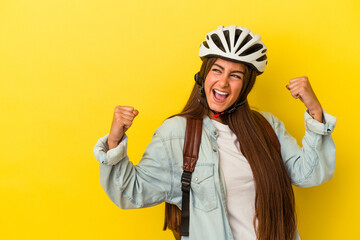 Young student caucasian woman wearing a bike helmet isolated on yellow background raising fist after a victory, winner concept.
