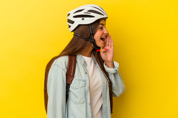Young student caucasian woman wearing a bike helmet isolated on yellow background shouting and holding palm near opened mouth.