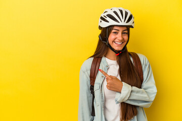Young student caucasian woman wearing a bike helmet isolated on yellow background smiling and pointing aside, showing something at blank space.