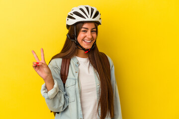 Young student caucasian woman wearing a bike helmet isolated on yellow background joyful and carefree showing a peace symbol with fingers.