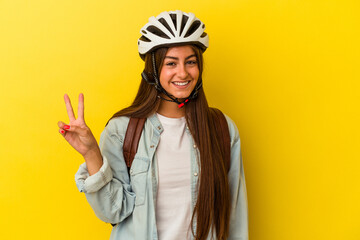 Young student caucasian woman wearing a bike helmet isolated on yellow background showing number...