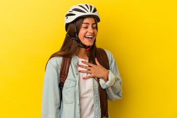 Young student caucasian woman wearing a bike helmet isolated on yellow background laughs out loudly keeping hand on chest.