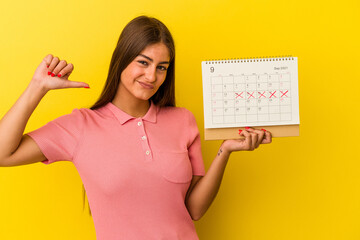 Young caucasian woman holding a calendar isolated on yellow background feels proud and self confident, example to follow.