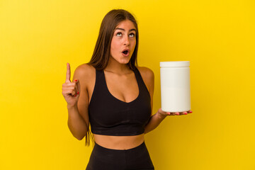 Young caucasian woman holding a protein bottle isolated on yellow background pointing upside with opened mouth.