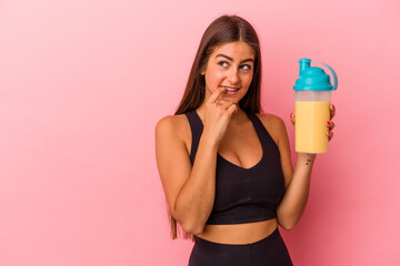 Young caucasian woman holding a protein shake isolated on yellow background relaxed thinking about...