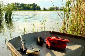 Fishing rod in a wooden boat on the background of the wild nature of the lake. Fishing on a sunny summer day on the lake. Bait, fishing rod fishing accessories in a boat. Rest outside the city