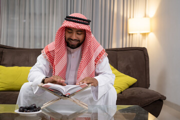 an Arab youth smiling while reading the Koran while sitting indoors