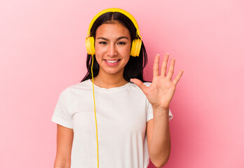 Young Venezuelan woman listening to music isolated on pink background smiling cheerful showing number five with fingers.