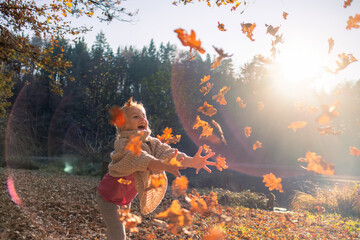 Smiling girl child throwing dry leaves in the air at beautiful autumn sunset.
