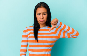 Young Venezuelan woman isolated on blue background showing a dislike gesture, thumbs down....