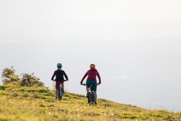 Mother and daughter cycling downhill with mtb bikes at a sunset.