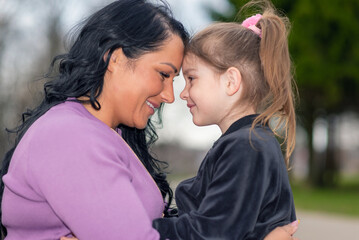 Fototapeta premium Profile shot cute girl and her mom touching with foreheads, at evening park outdoors.Summer evening,closeup shot.