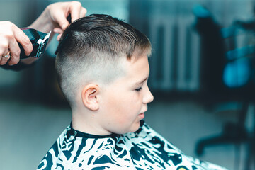 Cute kid have hair cut,professional barber doing haircut. Hairdress for children. side view portrait barbershop.Toned
