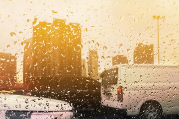 Many rain drops image on rainy season show urban area traffic jam with evening bright sunlight and blurry cars and buildings for meteoroloy presentation and transportation background.