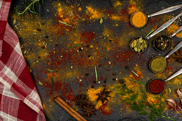 Spoons with spices, red towel, scattered spices on a black background.