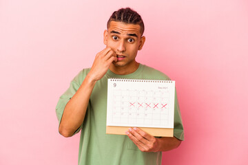 Young venezuelan man holding a calendar isolated on pink background biting fingernails, nervous and very anxious.