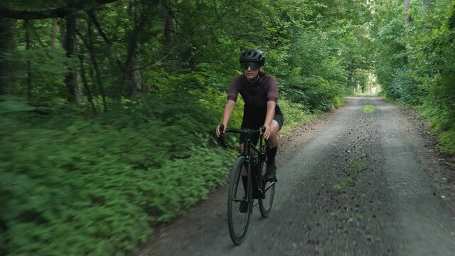 Gravel cycling. Woman riding bicycle in forest. Cyclist twists pedals on bike along gravel road