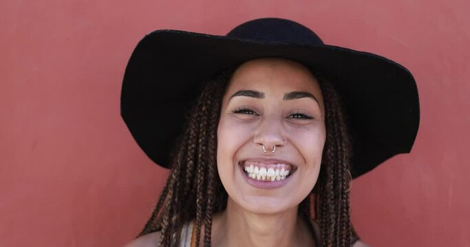Young african hipster woman with braids laughing on camera while wearing hat