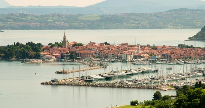 Elevated view of old town Izola in Slovenia. Adriatic Sea coast. Boats and yachts docket in marina. Panoramic static shot of Mediterranean settlement Isola. Sailboat leave the harbor. Static shot