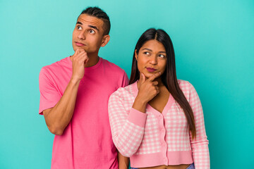 Young latin couple isolated on blue background looking sideways with doubtful and skeptical expression.