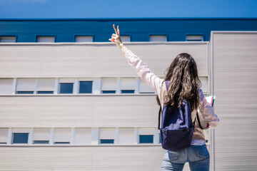 Student girl standing in front of college with the victory sign