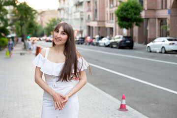 brunette girl with long hair in a white dress on a background of street in city. place for your design