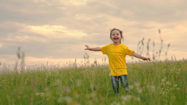 Happy child, girl runs raising her hands like flyer in green grass. Happy little girl dreams of flying in nature. Children's fantasies. Child running through field of flowers at sunset. Happy family.