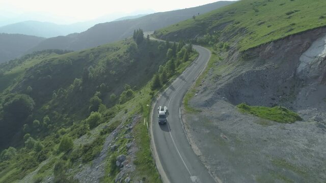 Drone follows blak SUV towing empty trailer on forest mountain road