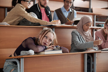 Bored female student looking at teacher while her groupmates working in team