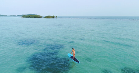 Aerial drone bird's eye view of man exercising sup paddle board in turquoise tropical clear waters, Thailand