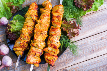 Baked barbecue chicken meat on skewers in a plate on a wooden table