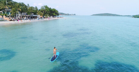 Aerial drone bird's eye view of man exercising sup paddle board in turquoise tropical clear waters,...