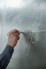 Hand of teacher with chalk by blackboard during explanation at algebra lesson