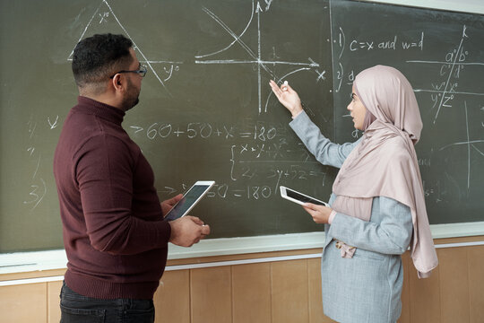 Young female student explaining graph to her teacher by blackboard