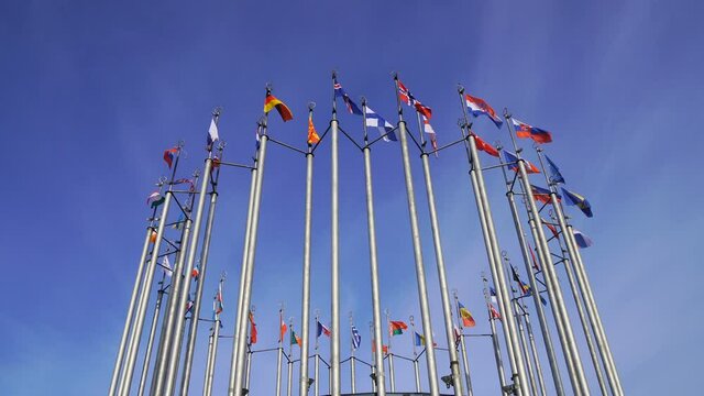 Many European country flags waving on flagpoles on windy day on blue sky background.