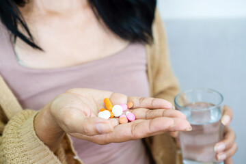 closeup handful of medicines, hand woman hand taking overdose pills with glass of water - obrazy, fototapety, plakaty