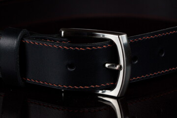 Black leather belt with a metal buckle on a dark background close-up.