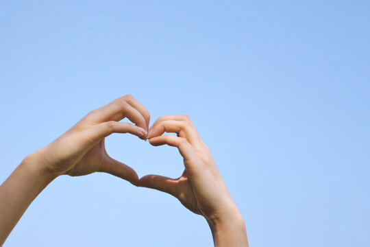 heart shape hand sign or love gesture against clear blue sky