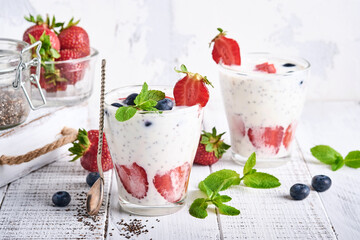 Two strawberry chia seeds layered smoothie or milkshake with strawberry and blueberry mint in glass on light grey background. Summer and healthy dieting drinks, vegetarian food concept.