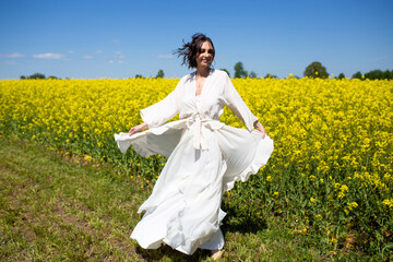 Naklejka na ściany i meble Beautiful Woman in white dress on Rape Field. Yellow Field. rapeseed plantation. Canola Field. Girl In Field.