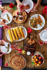 Top view over a dining table, decorated with flowers, with tableware and food. Backyard picnic with friends or neighbors, family dinner.