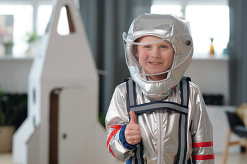 Cheerful little boy in space-suit showing thumb-up