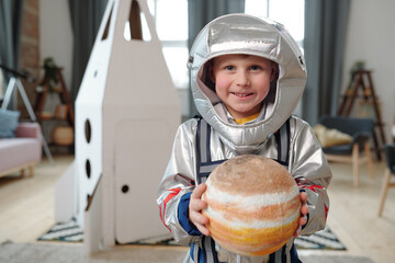 Adorable little boy in space-suit holding planet of solar system