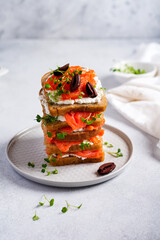 Sandwiches with smoked pink salmon olives, kalamata, microgreens and cream cheese on gray ceramic plate and trendy concrete background. Traditional Scandinavian toast. Top view