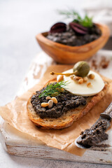 Sandwich with slice of mozzarella cheese and tapenade, caper on light grey rustic table background. Traditional Provence dish. Selective focus