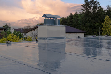 Flat roof covered with bitumen membrane and silver lacquer with chimney on a private house....