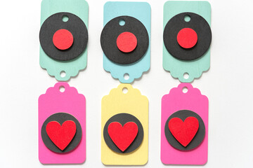 pastel colored wood chalkboard tags loosely arranged in a classic arragement with hand painted red hearts and black discs on a white paper background