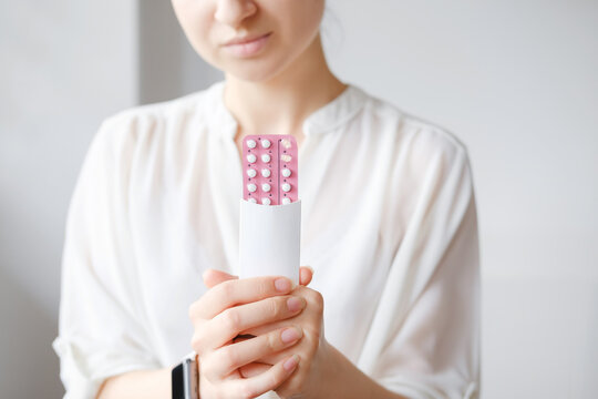 Unrecognized woman in white blouse holding hormonal oral contraceptives in a pink blister. Concept of Hormonal methods of birth control. Estrogen and Progestin hormonal balance.